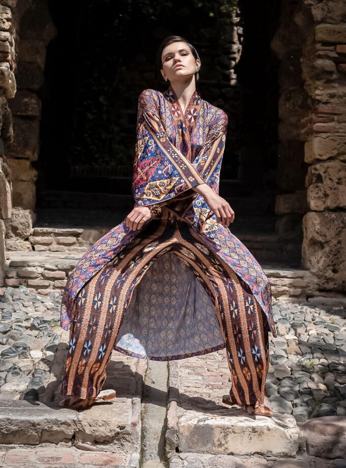 Junge Frau auf einem Fels stehend, in einem knielangen Kimono und weiter Hose mit armenischen Mustern aus der Mairik Kollektion von Belle Ikat