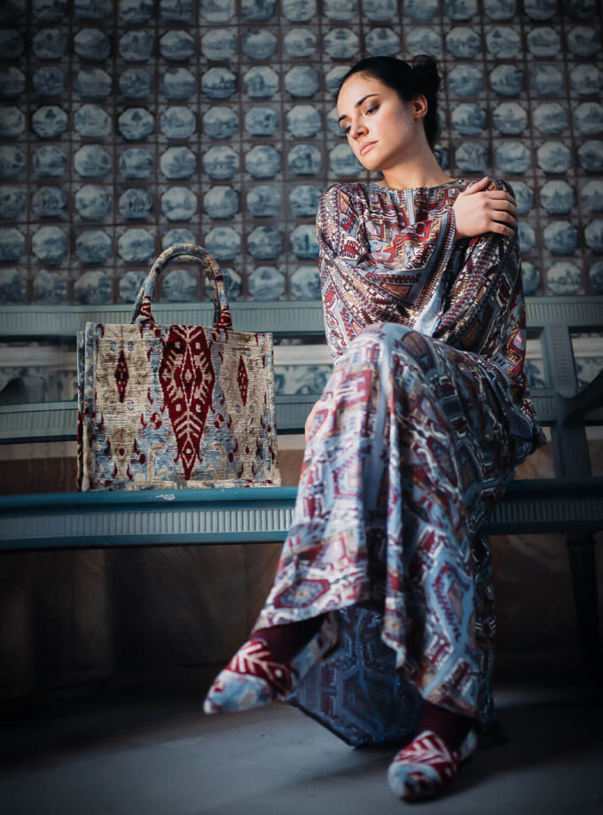 junge Frau sitzt auf einer Bank mit einer gemusterten Tote bag und Maxi Kleid mit armenischen Mustern