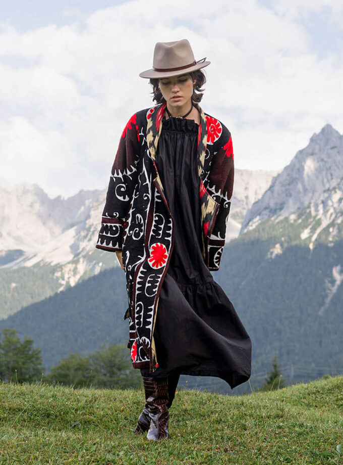 Berglandschaft mit junger Frau im Hut und einem schwarz-weiss-roten oversized Mantel mit Suzani-Stickereien